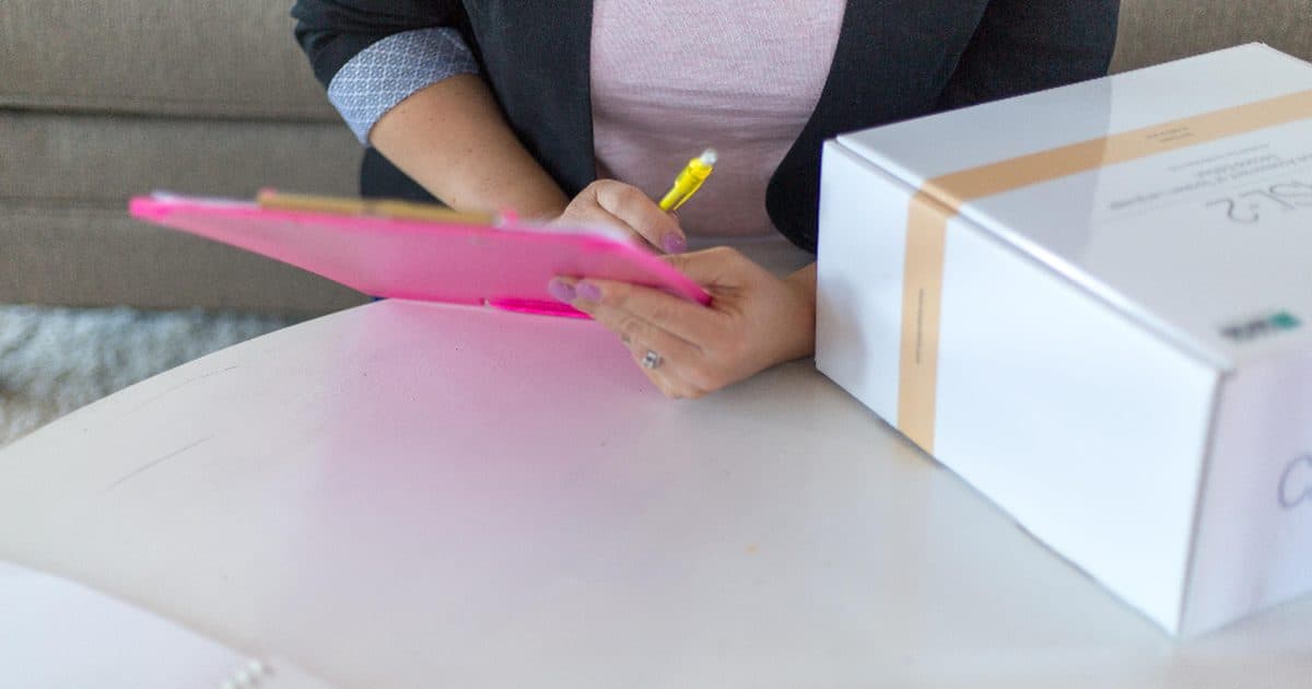 Hands writing on a clipboard next to a box