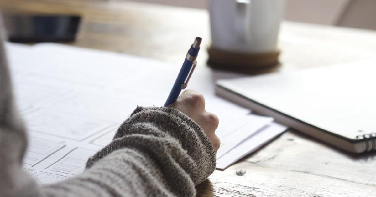 A hand writing on paper beside a coffee cup